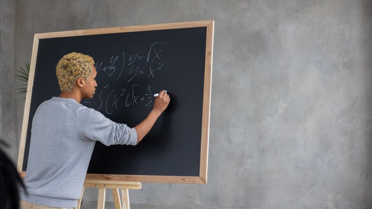 serious black student writing mathematical example on blackboard