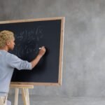 serious black student writing mathematical example on blackboard